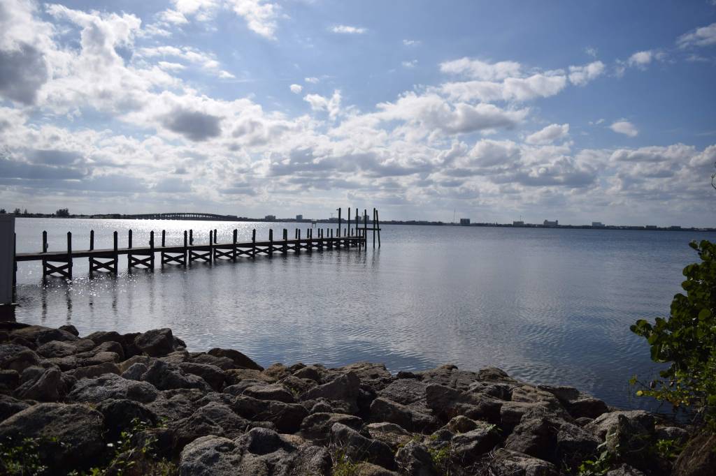 Mid afternoon view of the Indian River from Indialantic Florida. Rocks line the shoreline in the photo with a dock stretching out into the intracoastal river. In the distance is the Melbourne Causeway.