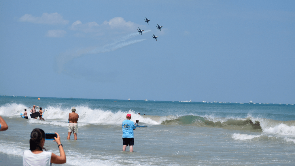 People in the ocean with waves breaking and the Thunderbirds flying overhead