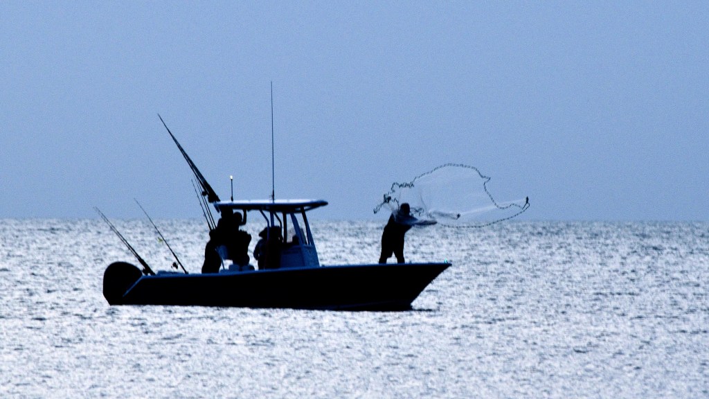 Fishing boat on the ocean throwing a cast net